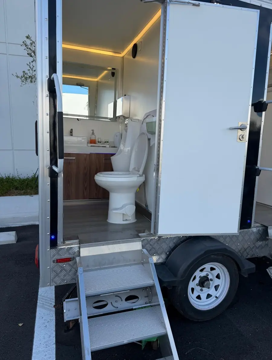 Open door of a luxury restroom trailer showing lighting and toilet