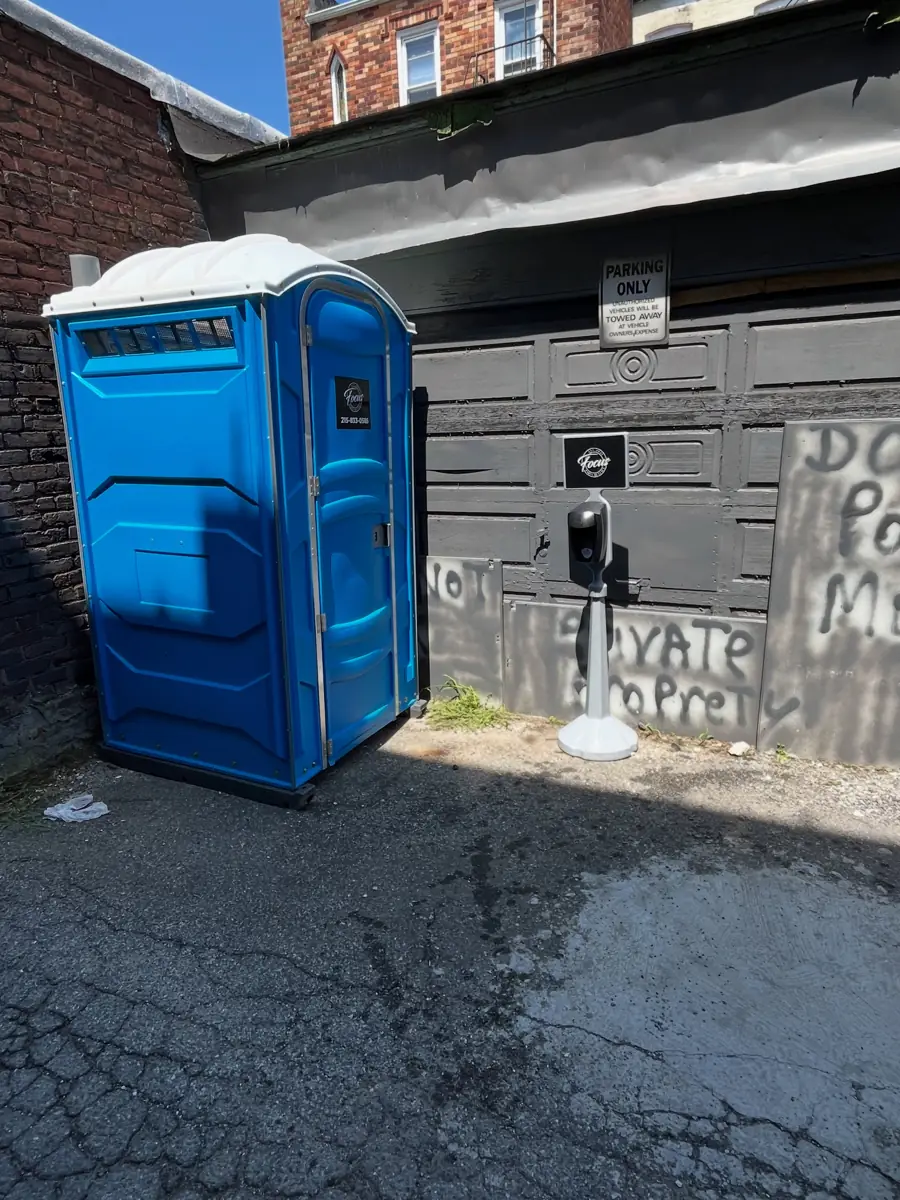 Blue porta potty placed on an asphalt driveway next to a garage