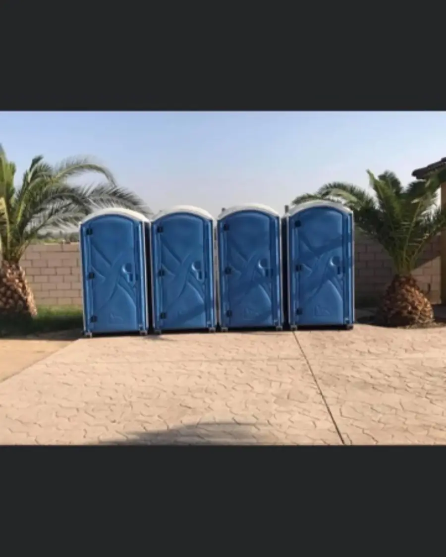 Four blue porta potties lined up on concrete between palm trees