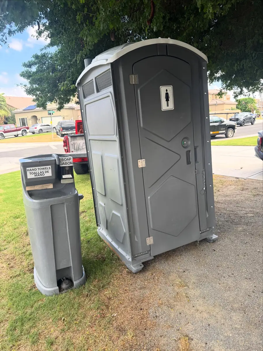Gray portable toilet with a foot-pump handwashing station on grass