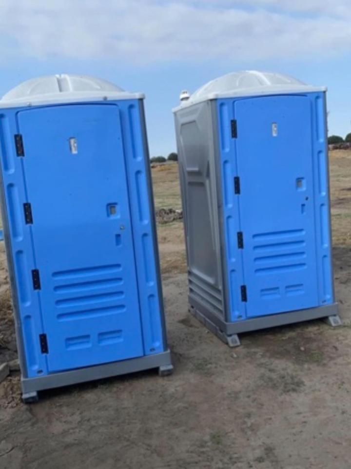 Two porta potties on a dirt construction lot under a clear sky