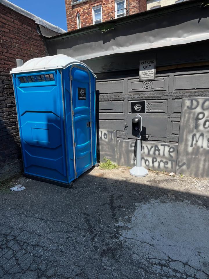 Blue porta potty placed on an asphalt driveway next to a garage